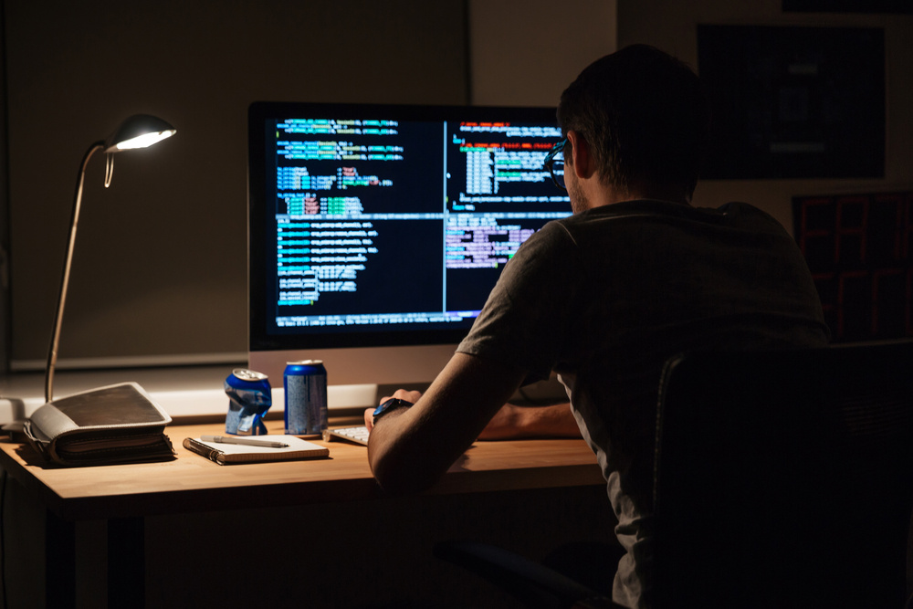 Back view of modern programmer sitting and writing code in dark room Back view of modern programmer sitting and writing code in dark room